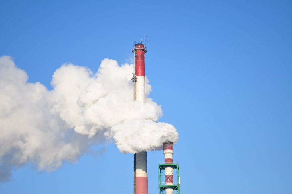 Photo of smoke stacks spewing carbon into a blue sky